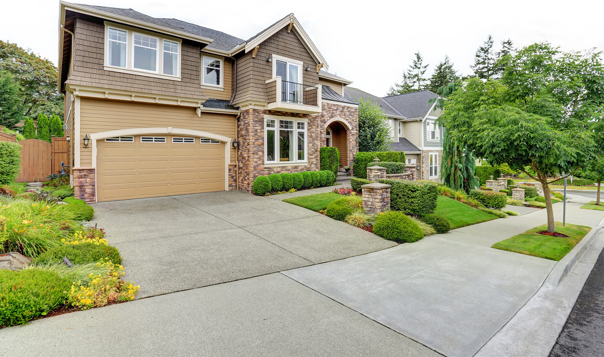 Two-story suburban house with a well-maintained yard, stone accents, and a two-car garage beside a neat sidewalk.