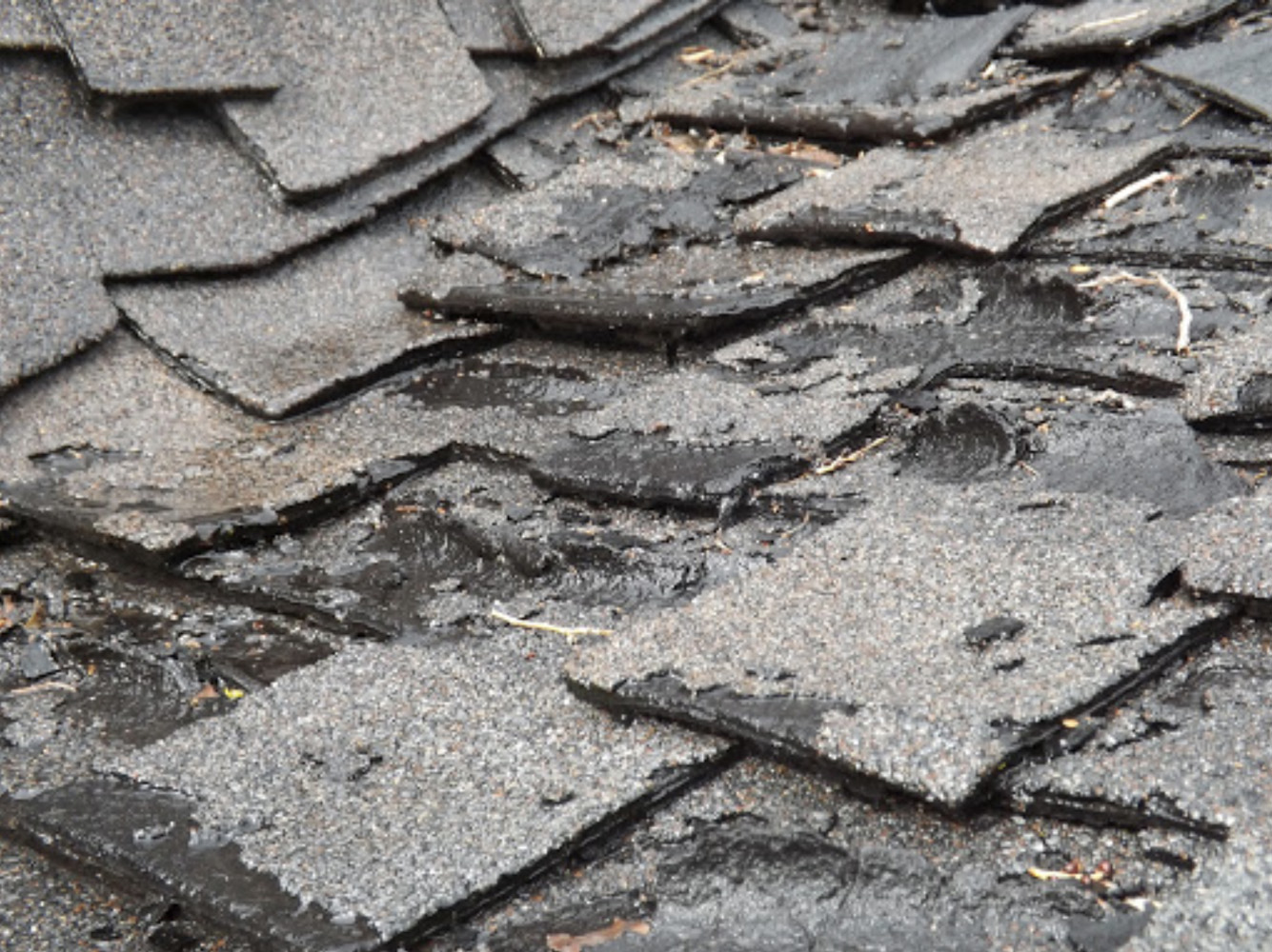 Close-up of a damaged, weathered roof with broken and curled asphalt shingles, showing signs of wear and need for repair.