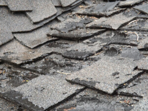 Close-up of a damaged, weathered roof with broken and curled asphalt shingles, showing signs of wear and need for repair.